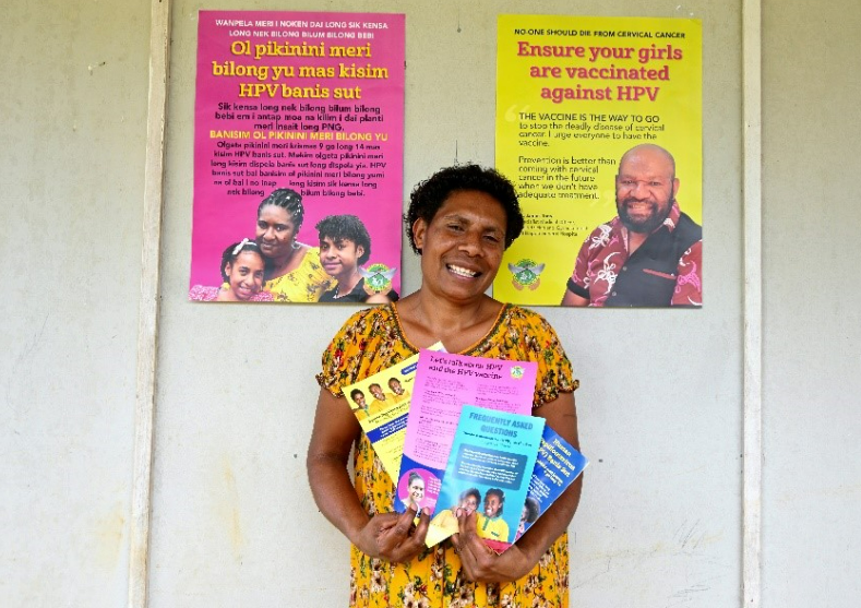 A PNG person holding immunisation education flyers, with educational posters stuck to the wall behind her.
