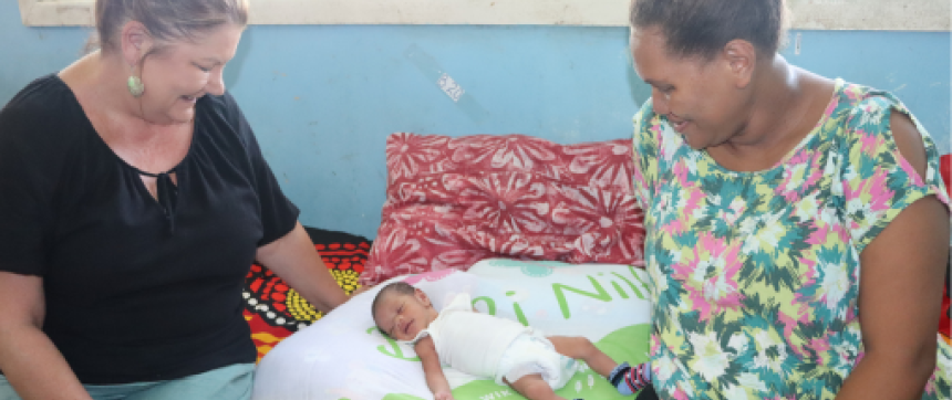 Baby lying on the swaddle blanket with carer and healthworker looking down at the baby